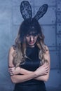Young blonde woman in black rabbit or hare fancy mask and black dress. Female on smoke and metal wall background Royalty Free Stock Photo