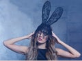 Young blonde woman in black rabbit or hare fancy mask and black dress. Female on smoke and metal wall background Royalty Free Stock Photo