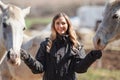 Young woman in black riding jacket standing near group of white Arabian horses smiling happy, one on each side, closeup detail Royalty Free Stock Photo