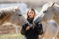 Young woman in black riding jacket standing near group of white Arabian horses smiling happy, one on each side, closeup detail Royalty Free Stock Photo