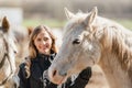 Young woman in black riding jacket standing near group of white Arabian horses smiling happy, one on each side, closeup detail Royalty Free Stock Photo