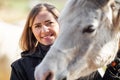 Young woman in black riding jacket standing near white Arabian horse smiling happy, closeup detail