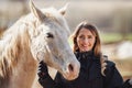 Young woman in black riding jacket standing near white Arabian horse smiling happy, closeup detail