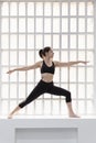 Young woman in black sportswear doing yoga pose next to a large window in her studio