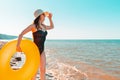 A young woman in a black swimsuit and a hat holding an orange swimming circle and looking into the distance .The sea in the Royalty Free Stock Photo