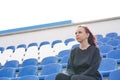 A young woman in a black tracksuit with long hair sits on the stadium stand alone and watches a sports game Royalty Free Stock Photo