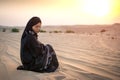 Young woman in black traditional clothes sitting on sand against sunset over desert Royalty Free Stock Photo