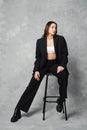 Young woman in black trendy pantsuit and ankle boots with rough sole sitting on tall stool Royalty Free Stock Photo