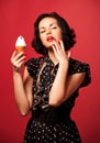 Young woman in black vintage dress standing eating ice cream over red background