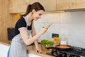 Young woman blogger in apron taking photo with phone while cooking food at kitchen. Preparing meal with frying pan on Royalty Free Stock Photo