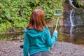 Young woman blogger in autumn mountains near lake and waterfall is recording video, taking photo with selfie stick Royalty Free Stock Photo