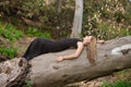 Young woman, blonde and beautiful, with a black dress, with her eyes closed, lying on the trunk of a big tree, in the middle of Royalty Free Stock Photo