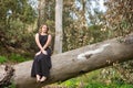 Young woman, blonde and beautiful, with a black dress, sitting on the trunk of a large tree, in the middle of nature, pure and Royalty Free Stock Photo