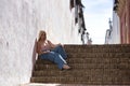 Young woman, blonde, green eyes, wearing pink top and jeans, sitting on a staircase, looking at the camera, relaxed and calm. Royalty Free Stock Photo