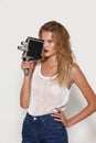 Young woman blonde posing in white fashion clothes in studio, make video with a retro camcorder.