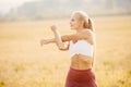 Young woman blonde in red pants and white T-shirt performs warm before running in park Royalty Free Stock Photo