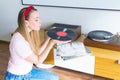 Young woman blowing dust off vinyl record and listening to music on turntable at home