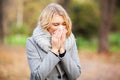 Young woman blowing her nose on the park. Woman portrait outdoor sneezing because cold and flu