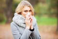 Young woman blowing her nose on the park. Woman portrait outdoor sneezing because cold and flu