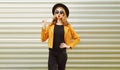 Young woman blowing red lips sending sweet air kiss wearing yellow jacket, black round hat on wall Royalty Free Stock Photo