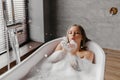 Young woman blowing soap bubbles and having fun while lying in bathtub full of foam at home, copy space Royalty Free Stock Photo