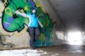 Young woman in blue anorak leaning against a graffiti wall