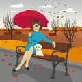 Young woman in blue autumn coat holding red umbrella sitting on a bench Royalty Free Stock Photo
