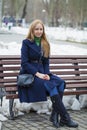 Young woman in a blue coat sitting on a bench in winter park Royalty Free Stock Photo