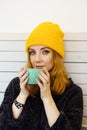 Young woman with blue eyes and blond hair in a yellow hat is drinking coffee in a cafe Royalty Free Stock Photo