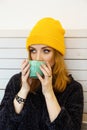 Young woman with blue eyes and blond hair in a yellow hat is drinking coffee in a cafe Royalty Free Stock Photo