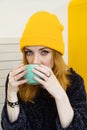 Young woman with blue eyes and blond hair in a yellow hat is drinking coffee in a cafe Royalty Free Stock Photo