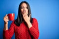 Young woman with blue eyes drinking cup of coffee standing over isolated background cover mouth with hand shocked with shame for Royalty Free Stock Photo