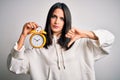 Young woman with blue eyes holding alarm clock standing over isolated white background with angry face, negative sign showing Royalty Free Stock Photo