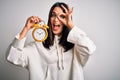 Young woman with blue eyes holding alarm clock standing over isolated white background with happy face smiling doing ok sign with Royalty Free Stock Photo