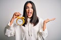 Young woman with blue eyes holding alarm clock standing over isolated white background very happy and excited, winner expression Royalty Free Stock Photo