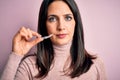 Young woman with blue eyes holding clear aligner standing over pink background with a confident expression on smart face thinking