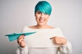 Young woman with blue fashion hair holding paper plane as travel symbol with surprise face pointing finger to himself Royalty Free Stock Photo