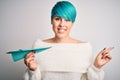 Young woman with blue fashion hair holding paper plane as travel symbol very happy pointing with hand and finger to the side Royalty Free Stock Photo