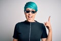 Young woman with blue fashion hair wearing thug life sunglasses over white background pointing finger up with successful idea