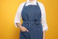 Young woman in blue jeans apron on yellow background, closeup Royalty Free Stock Photo