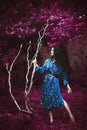 Young woman in blue kimono stand in infrared garden holding big white branch Royalty Free Stock Photo