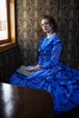 Young woman in blue vintage dress sitting with book in coupe of Royalty Free Stock Photo