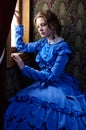 Young woman in blue vintage dress sitting in coupe near the win Royalty Free Stock Photo