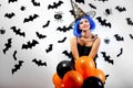 Young woman in a blue wig and witch`s hat black and orange balloons on a white background with black bats and spiders