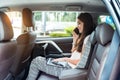 Young woman boss, top manager sitting in the back seat of luxury car and talking phone while working on laptop Royalty Free Stock Photo