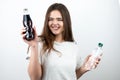 Young woman with bottle of soda drink in one hand and bottle of water in another biting her lipon isolated white background