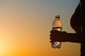 Young woman with bottle water after jogging on the sunset backgrounds. Top view on the city