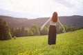 Young woman with a bouquet of flowers and wide open arms standing in the meadow. Forest and mountains in the background. Back view Royalty Free Stock Photo