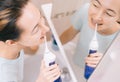 Woman with braces on her teeth brushing her teeth with by using a irrigate, before mirror, top view.