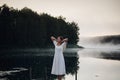 Young woman breathe deep while standing on a wooden pier on a sunrise in the morning at foggy lake